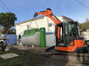 Excavatrice Hitachi soulevant une micro-station Tricel Filtro pour installation devant une maison.