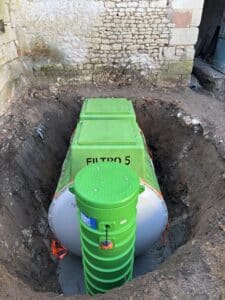 Installation d'un système Tricel Filtro 5 vert dans une fosse d'assainissement près d'un mur en pierre.